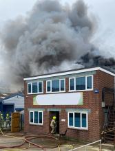 A firefighter in the doorway of a two-storey office style building, with smoke coming from the roof