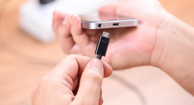 A hand holding a phone and the other hand placing a charger into the charging port