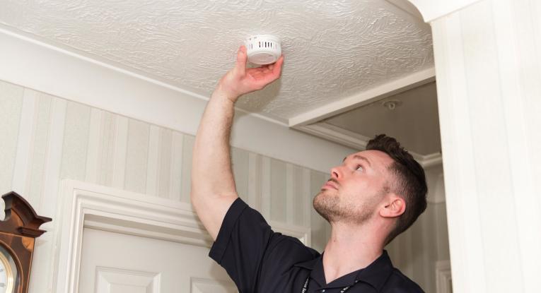Community Safety Officer fits smoke alarm to the ceiling