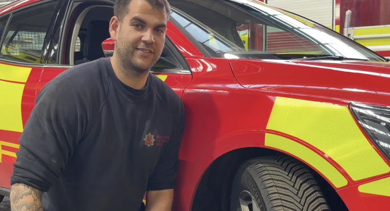 Tom Reed, an Engineer in our Fleet Workshops, in front of a red and yellow fire car. 