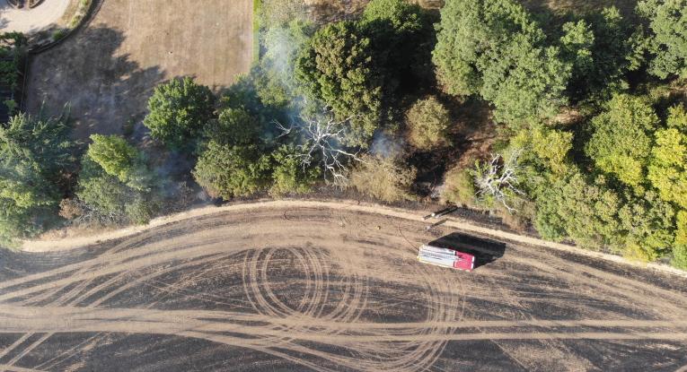 An aerial view of a burned field with a fire engine parked up.
