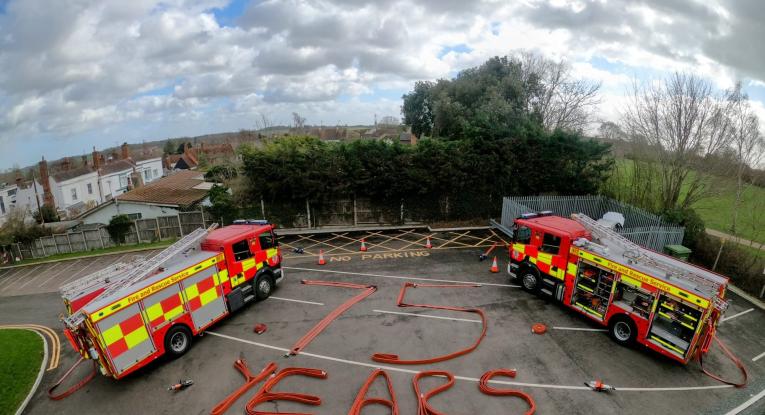 Two fire engines parked with '75 years' written using fire hoses. 