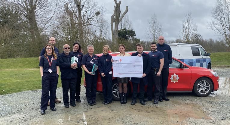 Members of the prevention team standing in front of a red car and holding a giant cheque