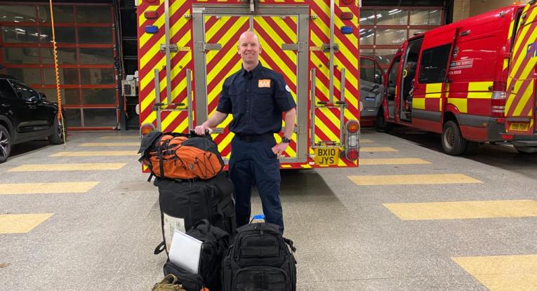 Firefighter Rob Thomson standing in front of a fire engine with his bags, ready to fly to Malawi