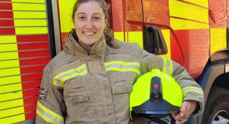 Firefighter Jennifer Adelle standing in front of a fire engine with her helmet