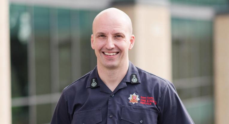 Chief Fire Officer Rick Hylton wearing a blue ECFRS shirt and standing in front of Fire HQ smiling at the camera