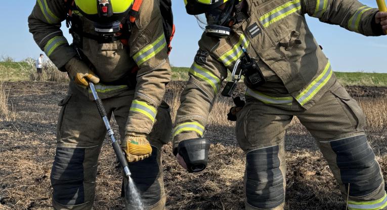 Two firefighters cooling a field after a wildfire